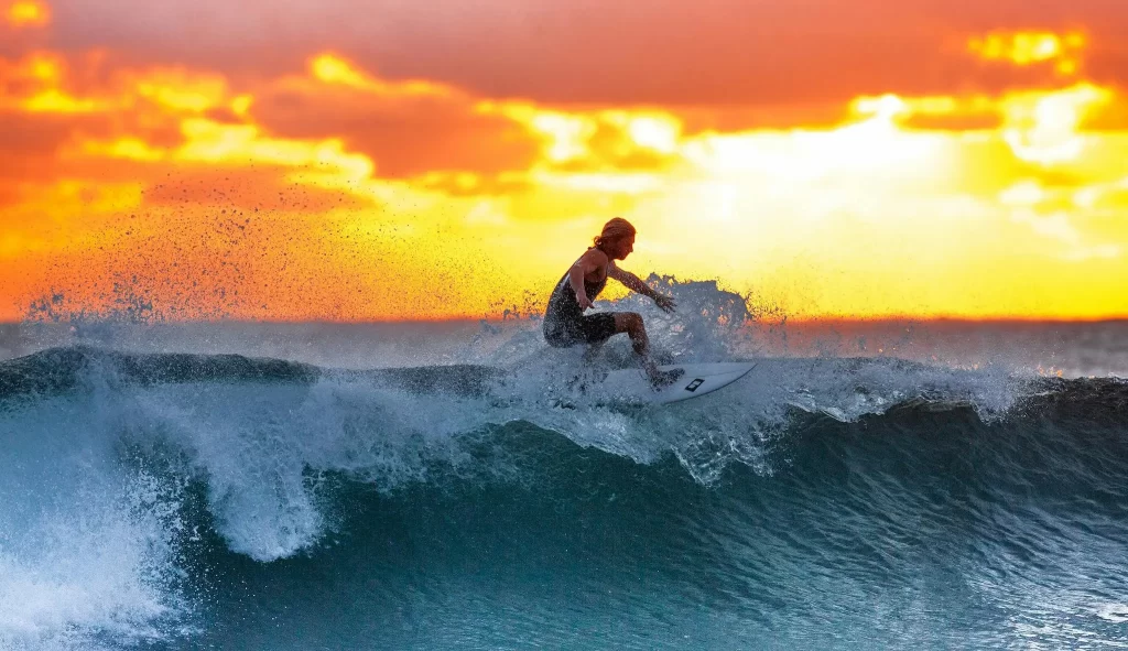 Surfer frozen mid-turn at sunset; fast shutter speed captures sharp water droplets.