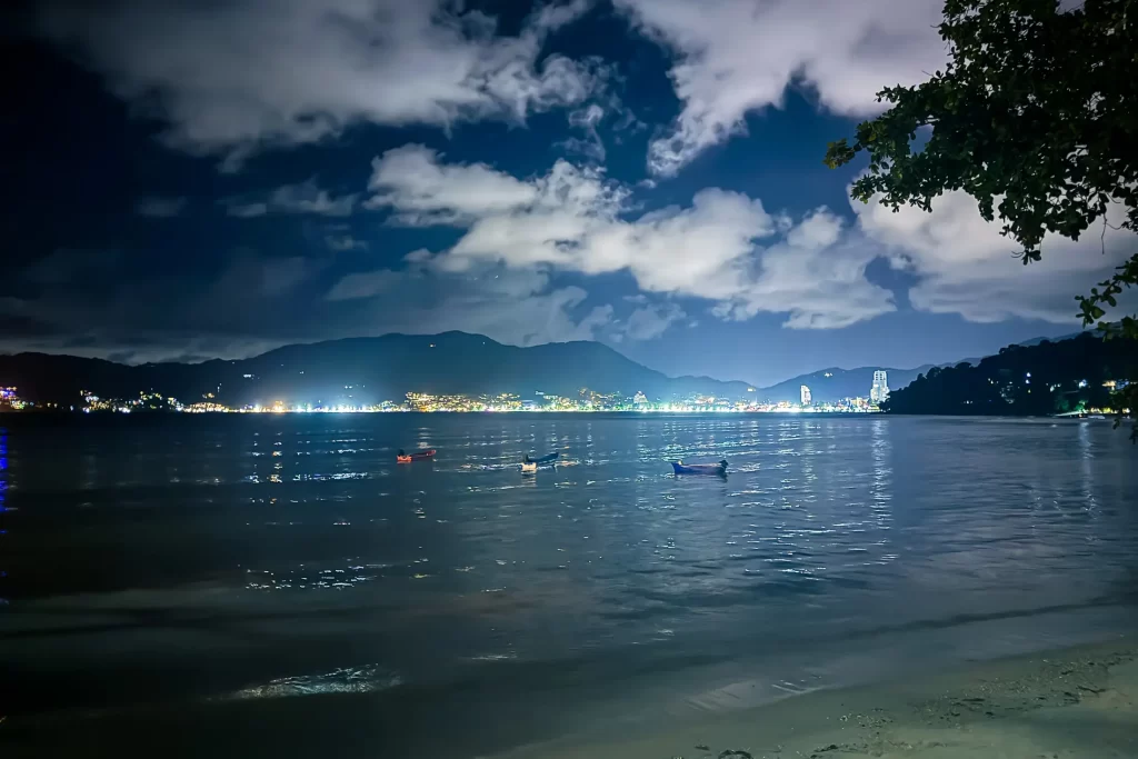 Night seascape of Patong Bay from Tri Trang Beach, Phuket—calm water, small boats, city lights.
