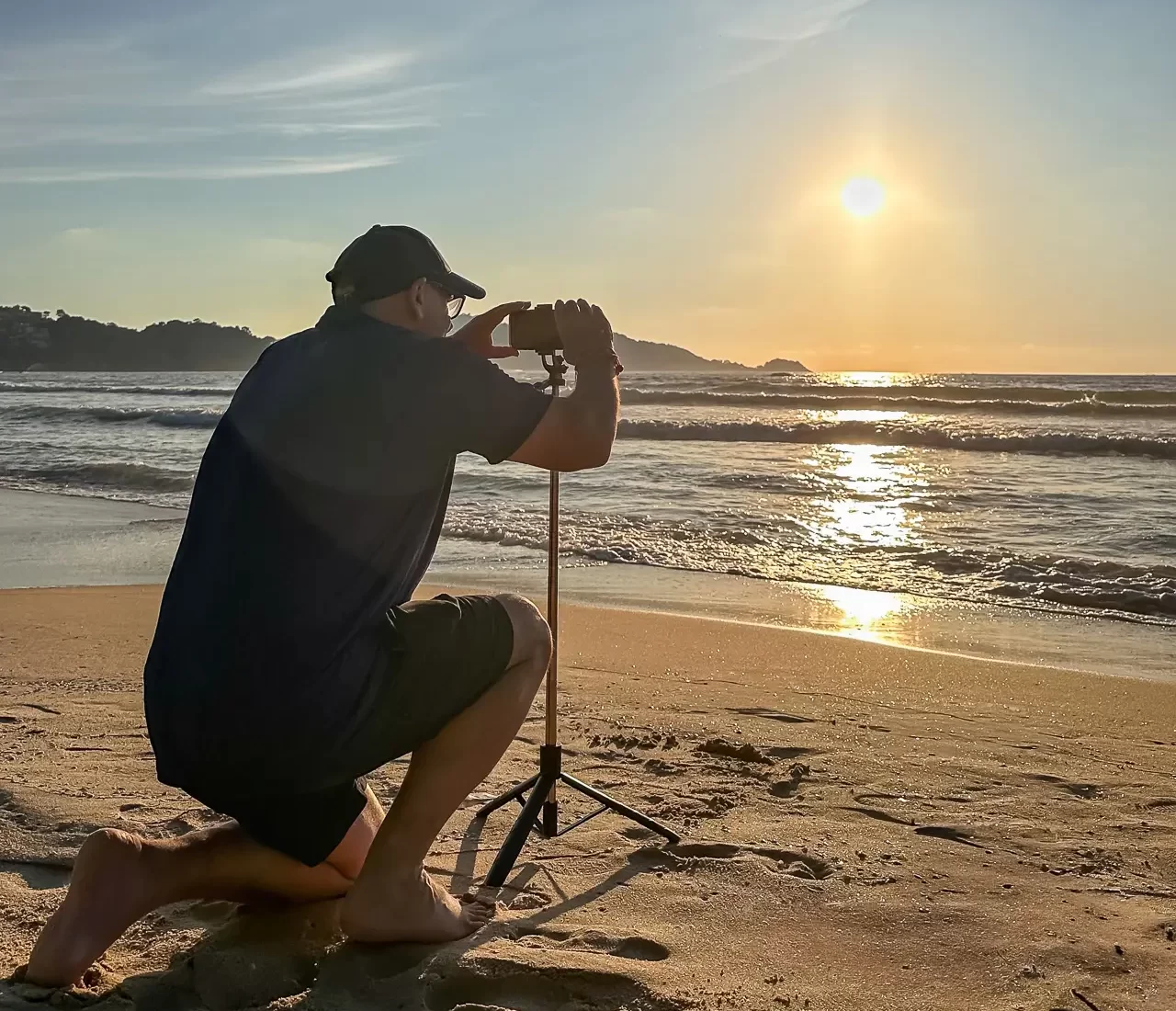 Dave Hibbins kneeling with a tripod on Patong Beach at sunset, photographing the surf.