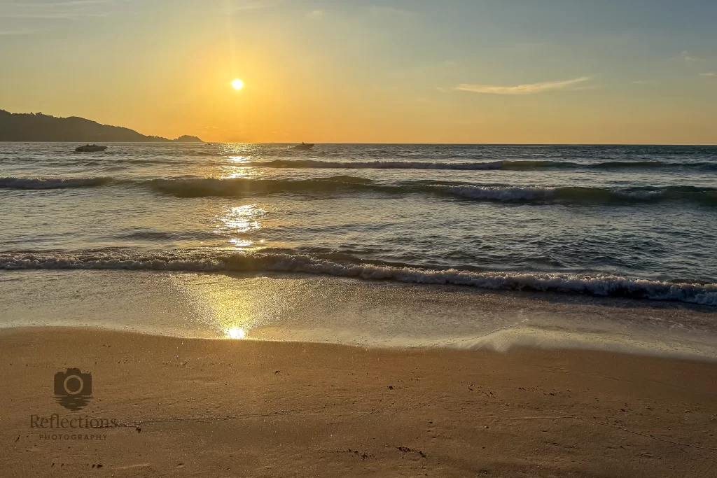 Patong Beach sunset reflection with gentle surf and sun path on wet sand, Phuket.