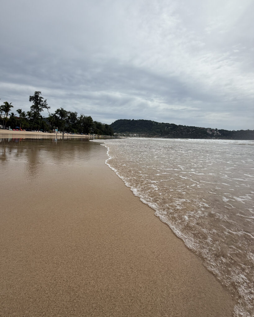 Serene morning reflection at Patong Beach, Phuket — calm sea, gentle waves, and wide sand under a soft overcast sky. Fine art beach photography by Reflections.