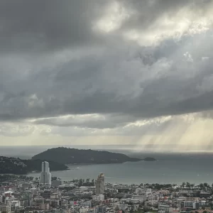 Sunbeams break through storm clouds over Patong Bay Phuket, lighting the Andaman Sea and coastal city below.