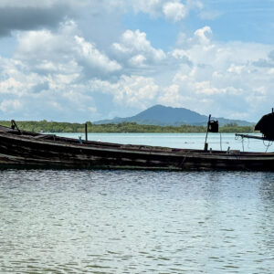Panoramic seascape of a Thai longtail boat near Sarasin Bridge, Phang Nga, with calm water, mountains, and bright clouds.