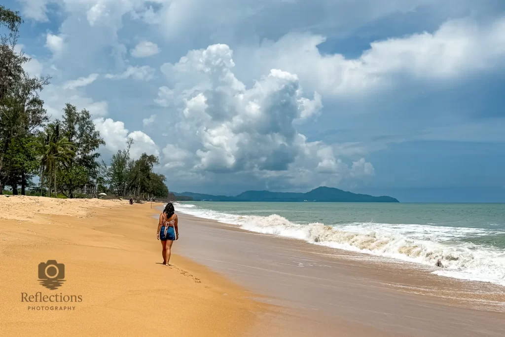 Woman walking along Sai Kaew Beach in Phang Nga, Thailand under dramatic clouds