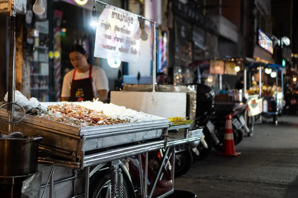 Street food cart at night on Soi Sansabai in Patong, Thailand, with seafood on ice and blurred market lights behind.