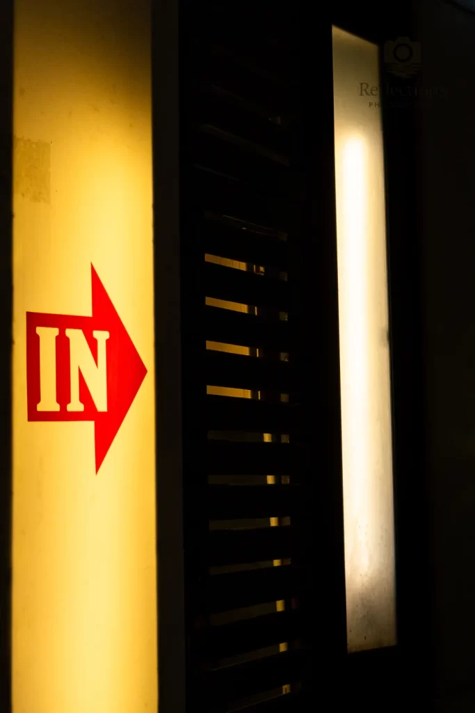 Red “IN” arrow sign on a wall at night in Patong, Phuket, with warm yellow panels and deep shadows.