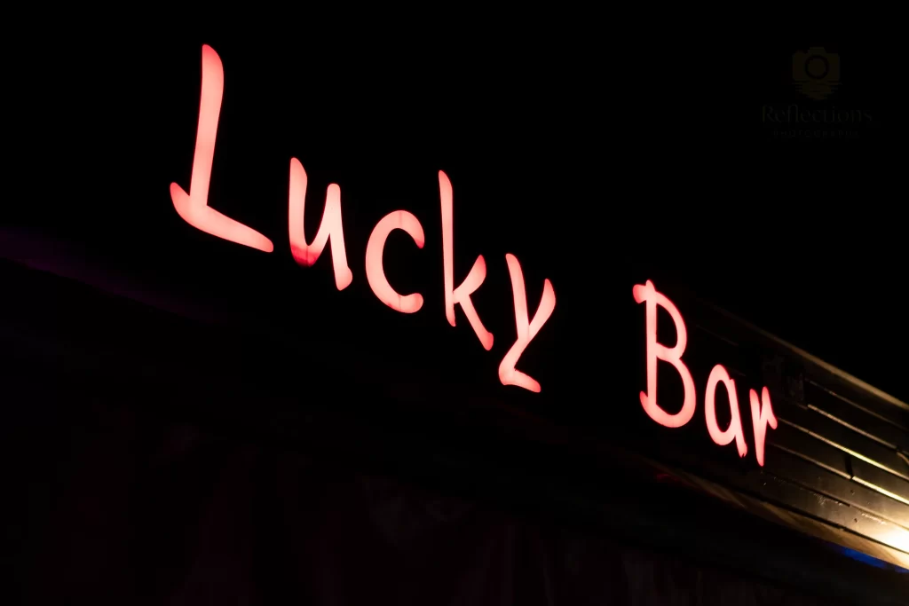 Neon “Lucky Bar” sign glowing in warm orange-pink light against the night sky in Patong, Phuket, Thailand.