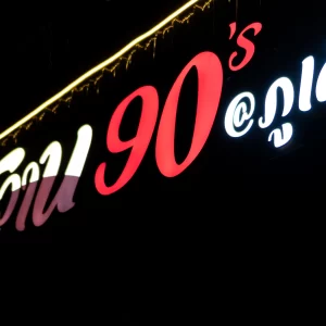 Bright thai neon sign 90s patong with glowing Thai script and red “90’s” numerals photographed at night against a dark background.