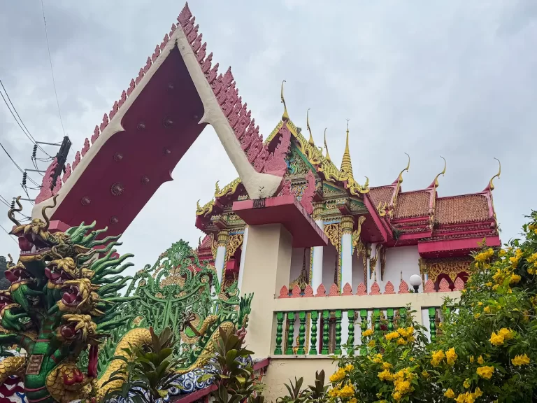 Dragon gate and yellow flowers framing Wat Suwan Khiri Wong temple buildings at Patong Hill, Phuket.
