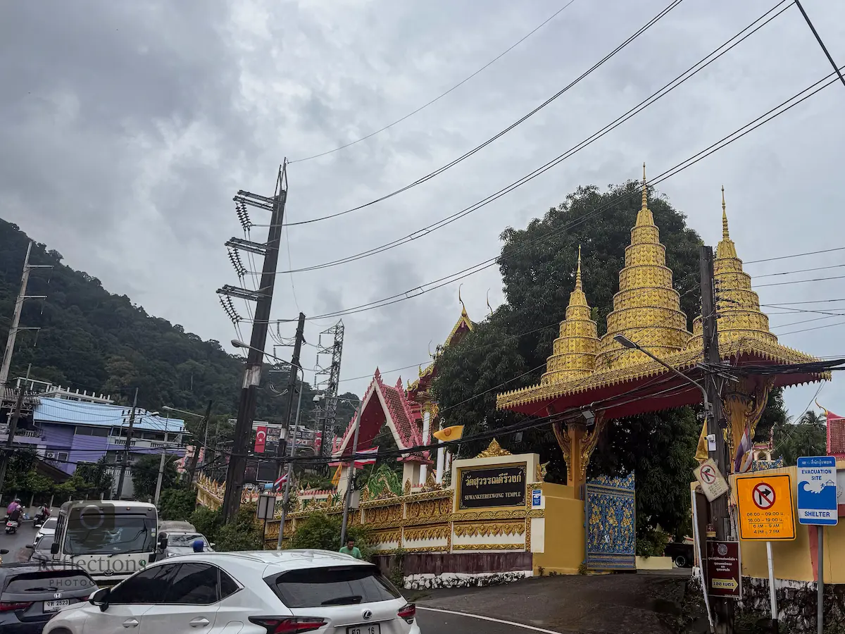 Main gate of Wat Suwan Khiri Wong Patong with ornate gold roof, temple wall signage, and busy road traffic outside