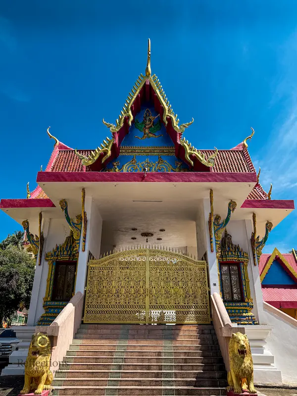 Viharn entrance at Wat Suwan Khiri Wong Patong with guardian lion statues, ornate gold gate, and raised steps