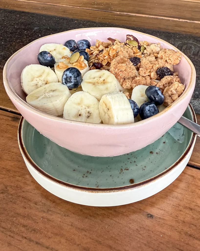 Close-up photo of a breakfast bowl with banana, blueberries and granola on a plate, framed tightly so the subject is clear.