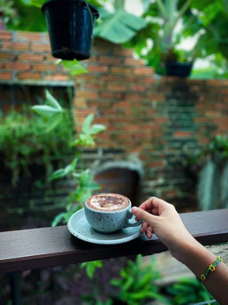 Hand holding a coffee cup on a balcony in a lush Thai garden – everyday creator lifestyle