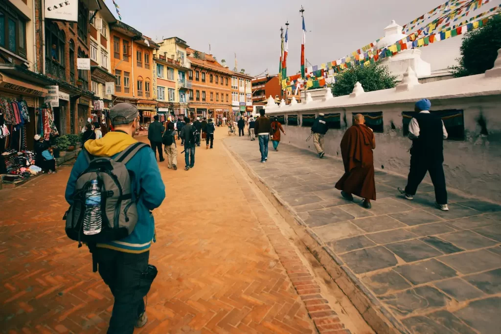 People walking past shops and prayer flags near Boudhanath Stupa in Kathmandu, Nepal.