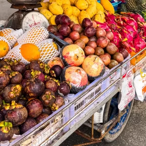 Colorful Thai fruit cart at a Patong street market with mangosteen, mangoes, dragon fruit and other tropical fruit piled on a metal cart.