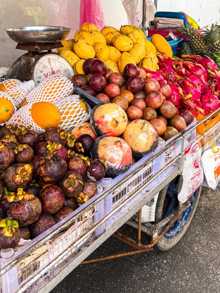 Colorful Thai fruit cart at a Patong street market with mangosteen, mangoes, dragon fruit and other tropical fruit piled on a metal cart.