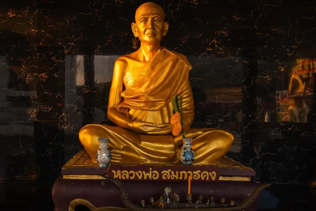 Golden monk statue inside Wat Suwan Khiri Wong Patong with offerings and subdued interior light