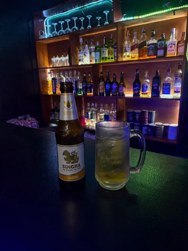 Beer bottle and glass on a bar counter photographed from a close position, with a busy background competing for attention.
