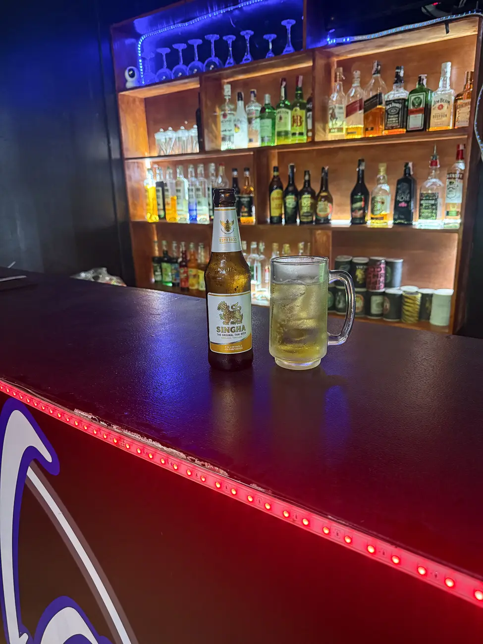 Beer bottle and glass on a bar counter photographed from slightly farther back, with more breathing room and cleaner edges.
