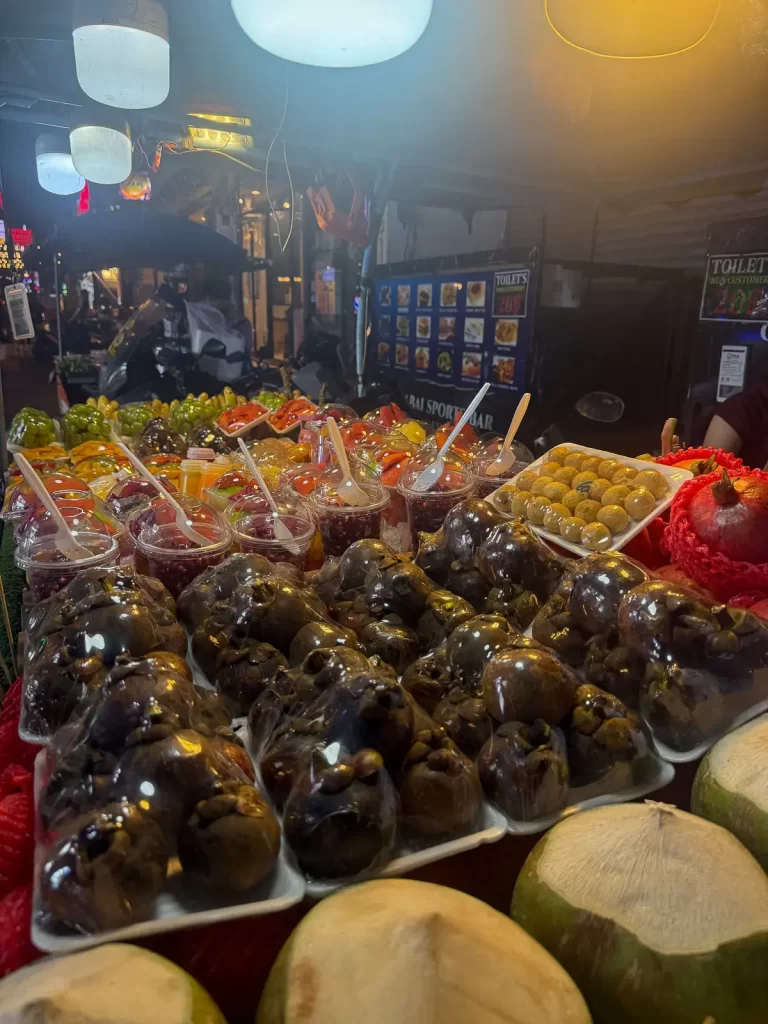 Street market photo where bright overhead lights pull attention away from the fruit in the foreground.