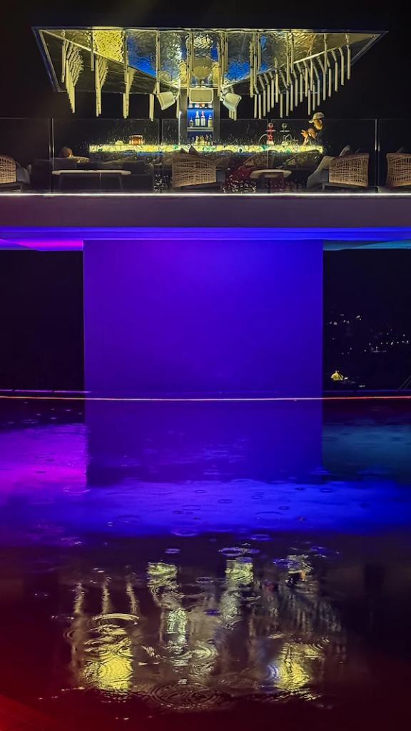 Rain-distorted reflection photography at Kipo Steakhouse in Kata, Phuket during light evening rain, showing atmospheric rooftop reflections interrupted by water ripples. Photo by Reflections Photography.