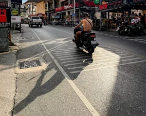 Documentary-style travel photography storytelling capturing a quiet afternoon street scene in Patong Phuket with long shadows and natural urban atmosphere