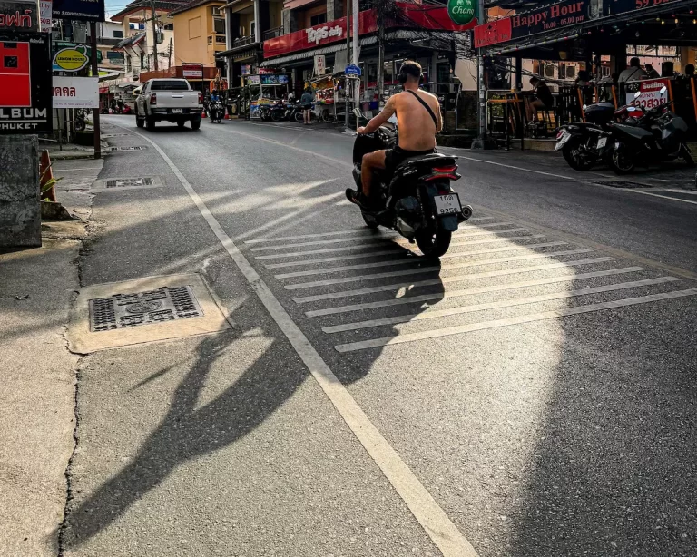 Documentary-style travel photography storytelling capturing a quiet afternoon street scene in Patong Phuket with long shadows and natural urban atmosphere