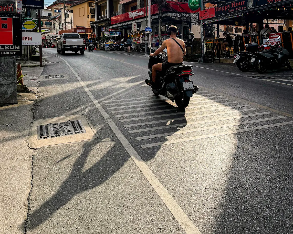 Documentary-style travel photography storytelling capturing a quiet afternoon street scene in Patong Phuket with long shadows and natural urban atmosphere