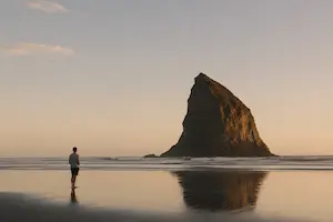 Minimal beach scene with a single person standing near a large rock formation at sunset demonstrating simplicity and visual clarity in photography