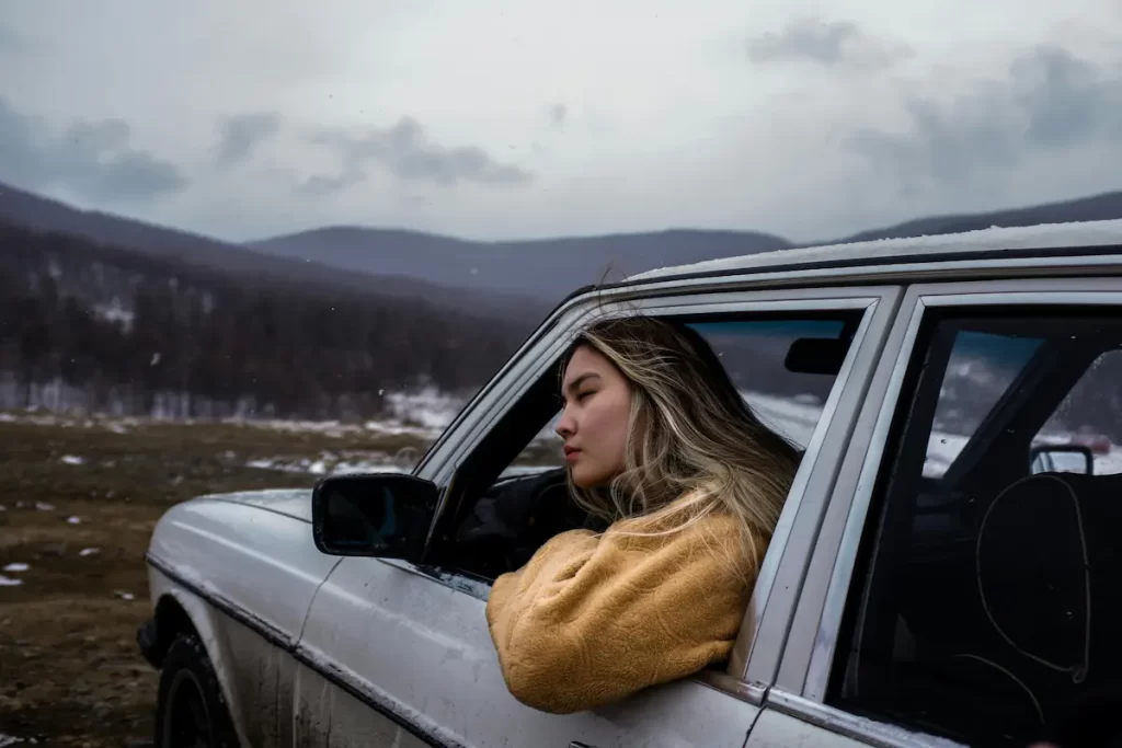 Environmental portrait of a woman leaning from a car window in a mountain landscape, used to explore environmental storytelling in photography and viewer interpretation.