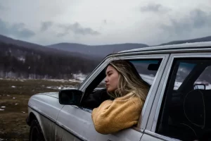 Woman resting in a car window against a cold mountain landscape, illustrating environmental storytelling in photography through atmosphere, mood, and emotional realism.