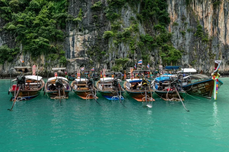 Longtail boats gathered in turquoise water beneath limestone cliffs in Thailand, demonstrating repetition, layering, and visual organisation in travel photography composition.