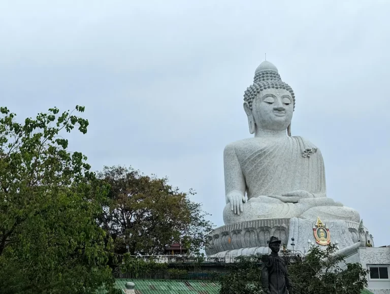 Large white Buddha statue photographed above surrounding trees and rooftops, illustrating travel photography framing and the balance between subject clarity and environmental context.